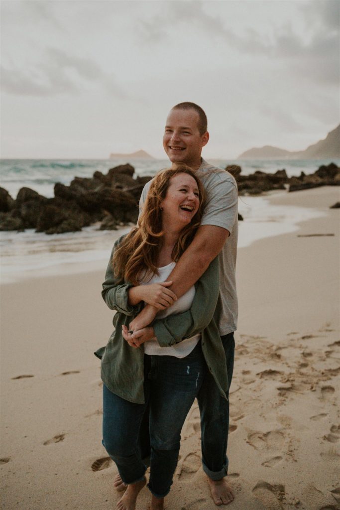 What to wear to your outdoor photoshoot. Couple standing on the beach hugging and laughing. 