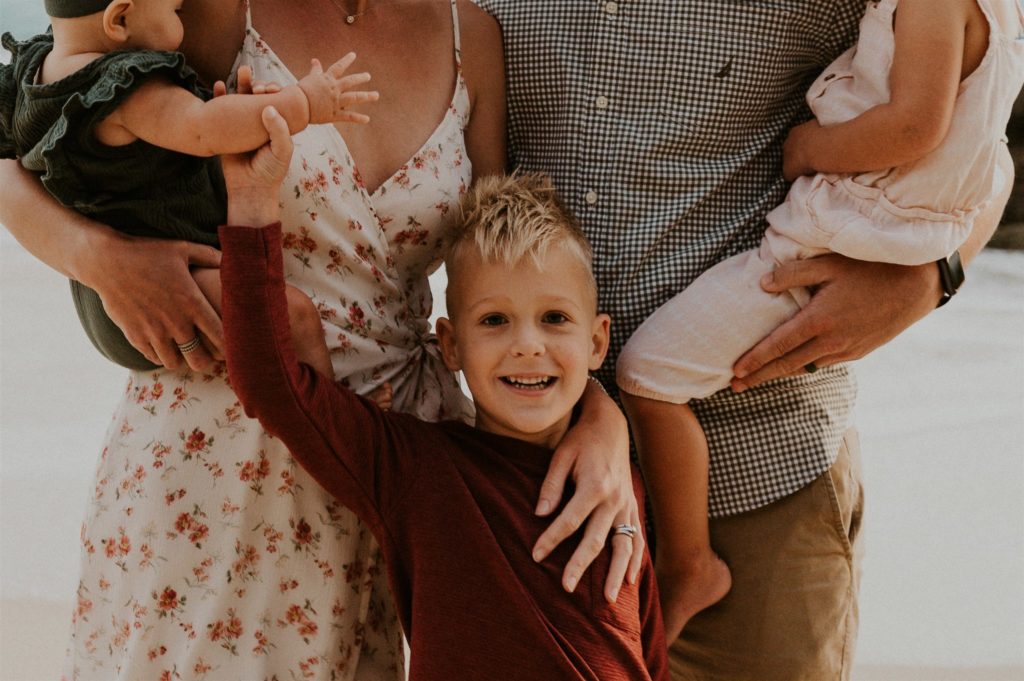 What to wear for family pictures. Little boy smiling at the camera while posing with his family.